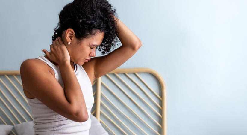 chica sentada en cama con dolor de cervicales